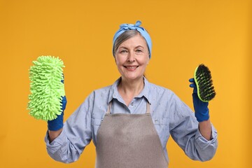Happy housewife with rag and brush on orange background