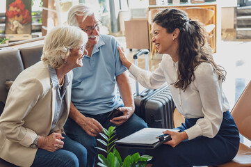 A hotel or travel agency representative is talking with a senior tourist couple offering various...