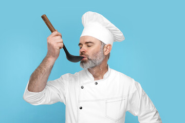 Chef in uniform tasting something on light blue background