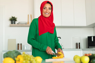 Woman wearing red and green hijab is skillfully cutting bell-pepper