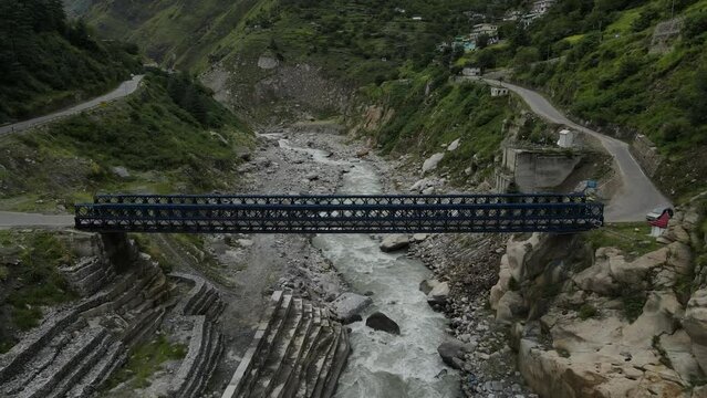 Aerial Drone Shot of a bridge above the flowing river in the mountains. 