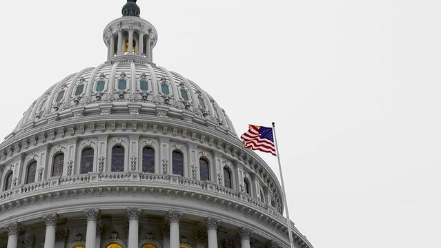 Low angle lockdown shot of American flag waving and capitol building against clear sky