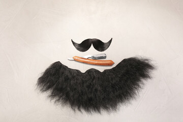 Artificial moustache, beard and straight razor on light background, flat lay