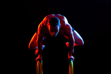 Front and side view photo of an strong young man exercising on parallel bars in studio.