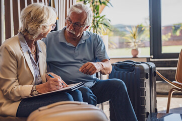 Senior couple checking into a hotel. Elderly couple sitting in a hotel lobby filling in forms....