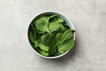Fresh spinach leaves in bowl on light textured table, top view