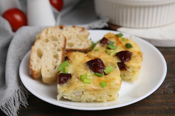 Tasty sausage casserole with green onion and bread on wooden table, closeup