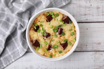Tasty sausage casserole with green onion in baking dish on white wooden table, top view