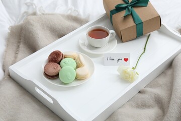 Tasty breakfast served in bed. Delicious macarons, tea, gift box, rose and I Love You card on tray