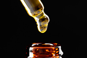 Dripping tincture from pipette into bottle on black background, closeup
