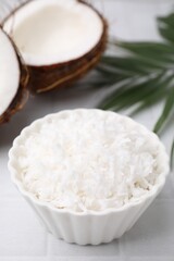 Coconut flakes in bowl, nuts and palm leaf on white table, closeup