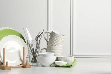 Beautiful ceramic dishware, cups and cutlery on white marble table, space for text