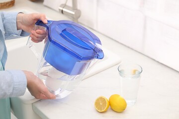 Woman with water filter jug in kitchen, closeup - obrazy, fototapety, plakaty