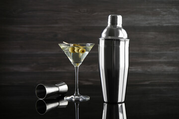 Metal shaker, Martini cocktail and jigger on black mirror surface