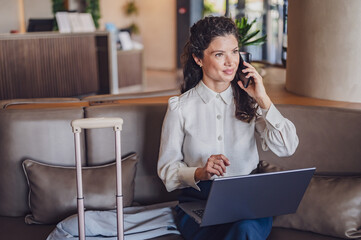 Businesswoman sitting in a hotel lobby, using laptop. Woman working on a business trip using online...