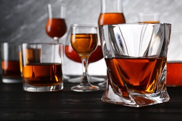 Different delicious liqueurs in glasses on dark wooden table - obrazy, fototapety, plakaty