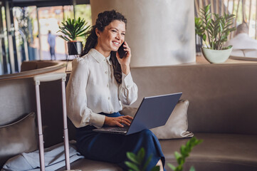 Businesswoman sitting in a hotel lobby, using laptop. Woman working on a business trip using online connections. Business lady went to business trip and stayed at the hotel.