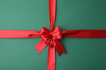Red satin ribbon with bow on green background, top view