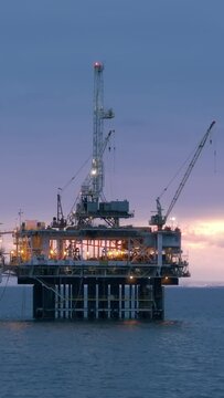 Vertical video. An oil rig towering over the ocean, extracting oil and natural gas from deep beneath the seabed. The rig is surrounded by vast expanses of water with no land in sight.