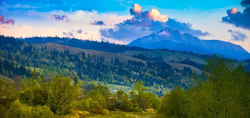 mountain sunset in the spring with Ceahlau peak in snow and green meadow on countryside of Romania...