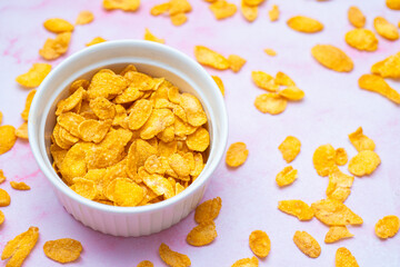 A top-down view of cornflakes in a bowl on a pink background. Flat lay image depicting breakfast preparation