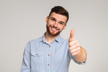 Portrait of handsome guy with thumb up on studio background
