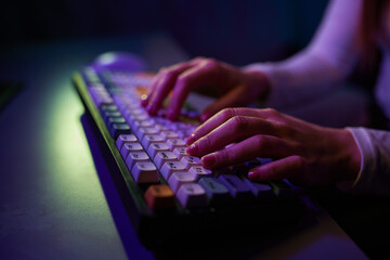 Professional online gamer hand fingers mechanical keyboard in neon color blur background.