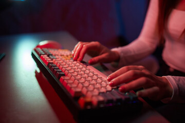 Professional online gamer hand fingers mechanical keyboard in neon color blur background.