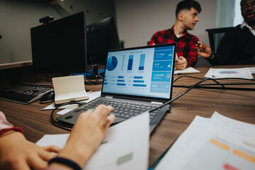 Multiracial team of young entrepreneurs engaged in a business meeting, analyzing project statistics and documents on a laptop in a well-equipped modern office.