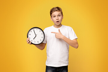 Surprised Boy Holding Clock Against Yellow Background