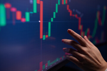 Finger to the graph on the monitor. Team of stockbrokers are having a conversation in a office with multiple display screens.