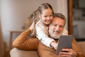 Man and Little Girl Sitting on Couch Viewing Tablet