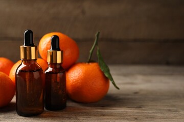 Bottles of tangerine essential oil and fresh fruits on wooden table. Space for text