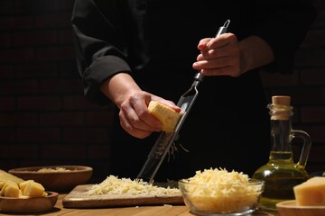 Woman grating cheese at wooden table, closeup - obrazy, fototapety, plakaty