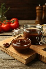 Tasty barbeque sauce in bowl, jar and spoon on wooden table