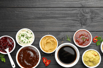 Different tasty sauces in bowls, parsley, chili pepper and rosemary on black wooden table, flat lay. Space for text