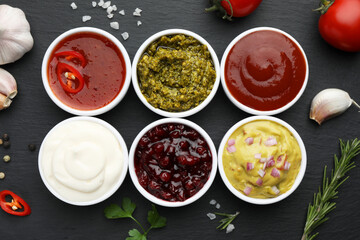 Different tasty sauces in bowls and ingredients on black table, flat lay