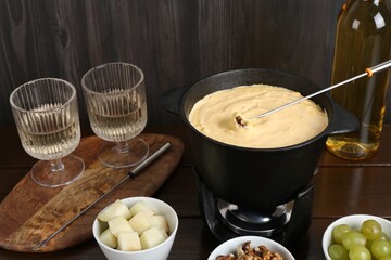 Fondue pot with tasty melted cheese, forks, wine and different snacks on wooden table