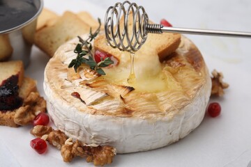 Pouring honey onto tasty baked camembert with thyme on white table, closeup