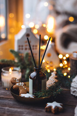 Xmas spirit, simple way to creating holiday atmosphere and festive mood at home on the window sill. Scented burning aromatic candles on wooden tray, liquid reed diffuser with sticks, fir tree branch