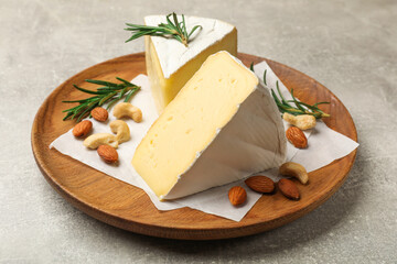 Plate with pieces of tasty camembert cheese, nuts and rosemary on grey textured table, closeup