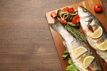 Delicious baked fish and vegetables on wooden table, top view. Space for text