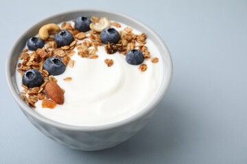 Bowl with yogurt, blueberries and granola on light grey background, closeup. Space for text