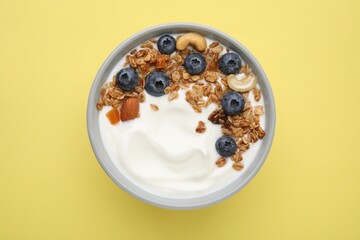 Bowl with yogurt, blueberries and granola on yellow background, top view