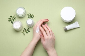 Woman applying hand cream on green background, top view