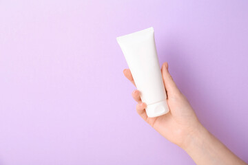 Woman with tube of cream on lilac background, closeup