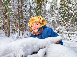 Funny boy in the snow in a snowdrift in a Russian hat with earflaps. Child is playing at war. A future soldier. The war between Russia and Ukraine