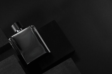 Stylish presentation of luxury men`s perfume in bottle on black background, top view. space for text