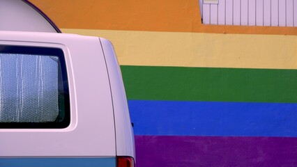 Camper van parked in front of rainbow painted wall. LGBT pride month concepts