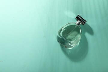 Luxury perfume in bottle on turquoise background, top view. Space for text